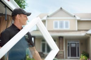 Are Fibrex Windows Worth the Cost Renewal by Andersen craftsman wearing black polo and cap is carrying a white-frame picture window.