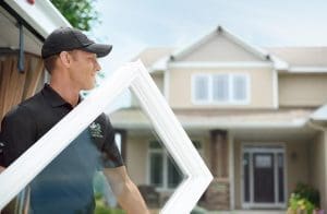 Renewal by Andersen craftsman wearing black polo and cap is carrying a white-frame picture window.