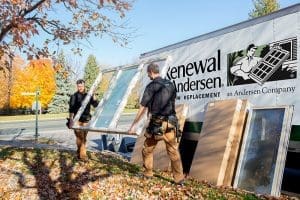 Two window installers carrying a replacement window out of a Renewal by Andersen truck.