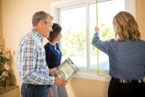 Couple looking at a gliding window while another individual measures the window with a measuring tape.