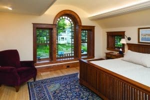 Custom Windows Minocqua WI Cozy bedroom with wood floors, wood-framed bed, and custom wood-framed windows that overlook a backyard.