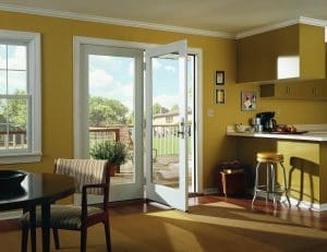 Spacious kitchen with wood flooring, golden yellow walls, and white hinged patio doors that lead to a deck.