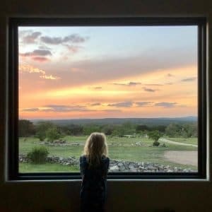 Young lady peering at the outdoor landscape through a large picture window