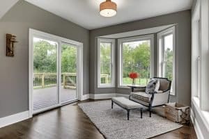 Selecting Windows for New Homes Residential indoor living area featuring wood flooring, a single chair and ottoman, and large frameless windows outlooking the backyard.